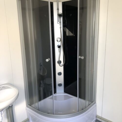 Contentor sanitário com chuveiro, lavatório e sanita.