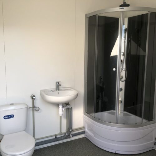 Contentor sanitário com chuveiro, lavatório e sanita.