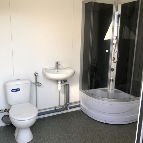 Contentor sanitário com chuveiro, lavatório e sanita.