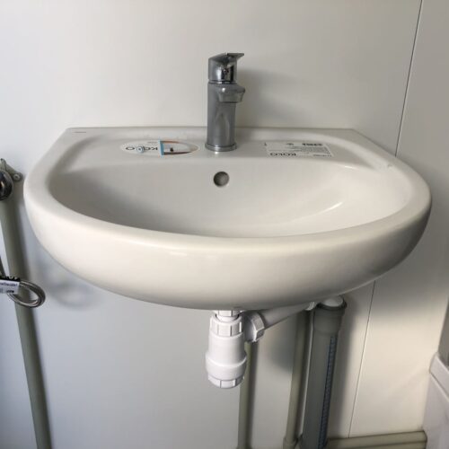 Contentor sanitário com chuveiro, lavatório e sanita.
