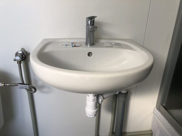 Contentor sanitário com chuveiro, lavatório e sanita.