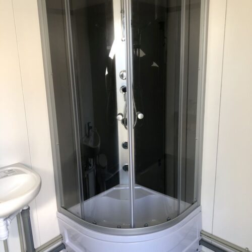 Contentor sanitário com chuveiro, lavatório e sanita.