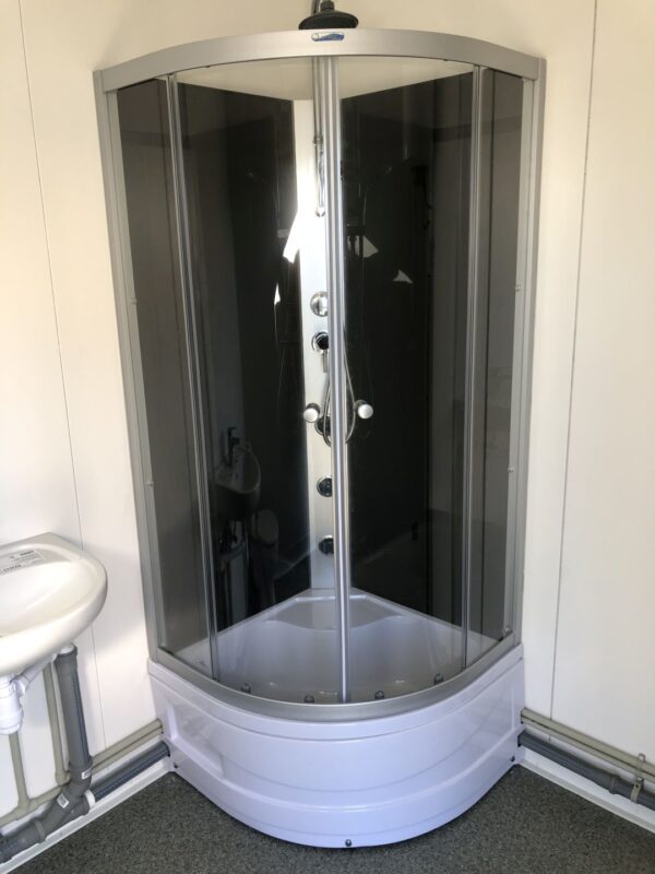 Contentor sanitário com chuveiro, lavatório e sanita.